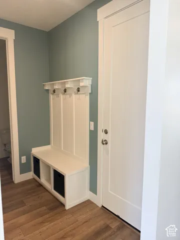 Built-in mudroom bench with storage cubbies and coat hooks, wood-finish flooring, and a white panel door