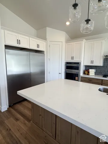 Kitchen featuring a large center island with a light-toned countertop, wood-finish flooring, white cabinetry with black hardware, and stainless steel appliances