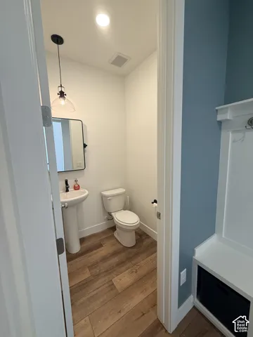 Pedestal sink, wood-finish flooring, black-framed mirror, contemporary pendant lighting, and built-in bench seating