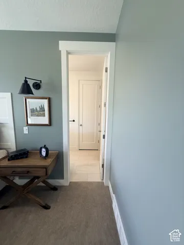 Carpeted room with a doorway featuring white trim and a flat panel door, opening to a space with tile flooring