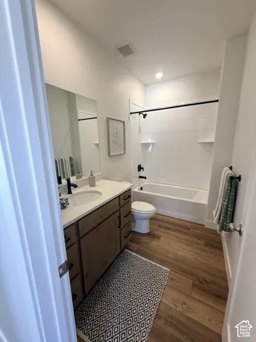 Wood-finish flooring, single vanity with light countertop, built-in bathtub with shower, and modern black fixtures