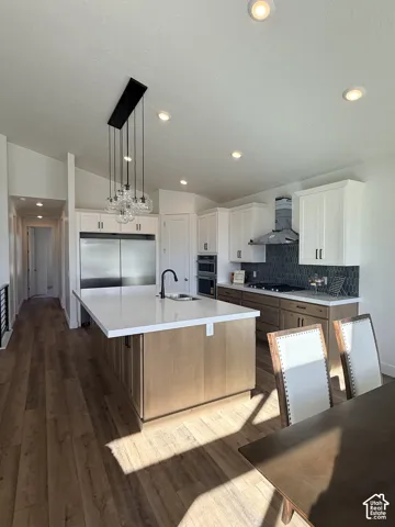 Open-concept kitchen featuring wood-finish flooring, a central island with a white countertop and integrated sink, stainless steel appliances, and a decorative pendant light fixture