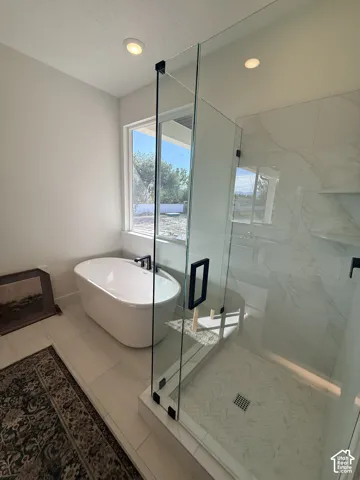 Freestanding soaking tub, glass-enclosed shower with herringbone tile, recessed lighting, and large format floor tiling