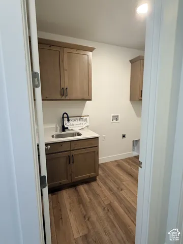Laundry area featuring wood-finish flooring, light-toned cabinetry with dark hardware, a sink with a black faucet, and a light-toned countertop