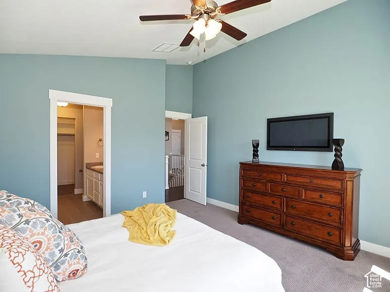 Vaulted ceiling featuring a ceiling fan with integrated lighting, wall-mounted television, and direct access to a bathroom with a vanity and mirror
