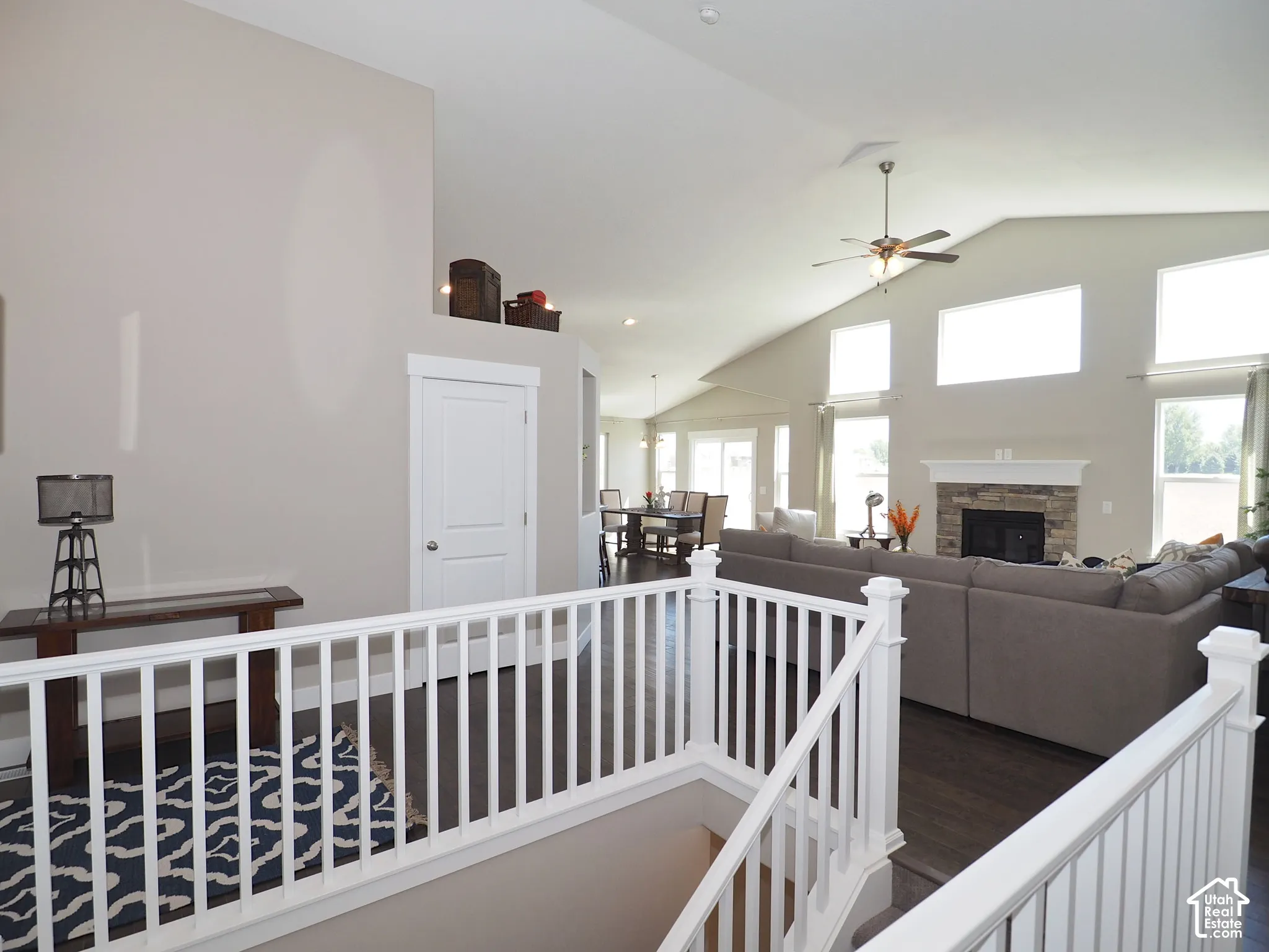 Vaulted ceiling living area with a stone fireplace, wood-finish flooring, and multiple large windows