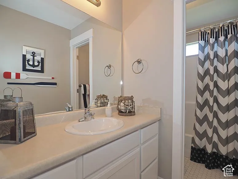 Vanity with an integrated sink and light-toned countertop, white cabinetry with silver-tone hardware, and a tub with white hexagonal tile flooring