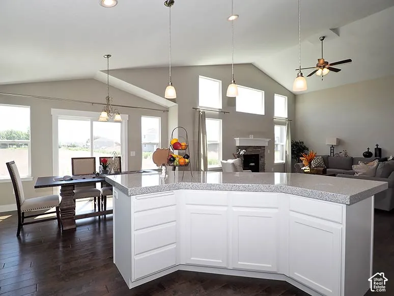 Vaulted ceilings, wood-finish flooring, white cabinetry, recessed lighting, and a stone fireplace