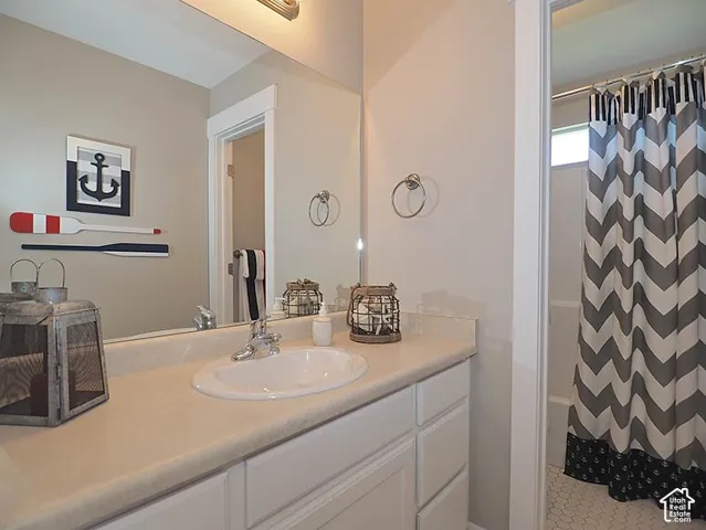 Vanity with an integrated sink and light-toned countertop, white cabinetry with silver-tone hardware, and a tub with white hexagonal tile flooring