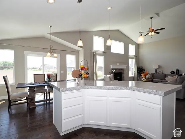 Vaulted ceilings, wood-finish flooring, white cabinetry, recessed lighting, and a stone fireplace