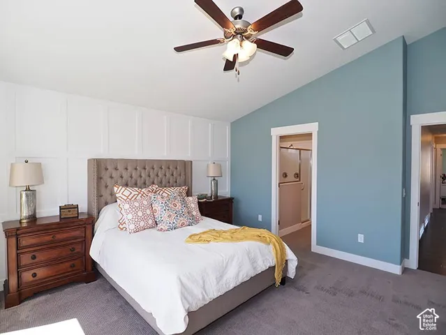 Vaulted ceiling with a ceiling fan, accent wall with wainscoting, and carpet flooring