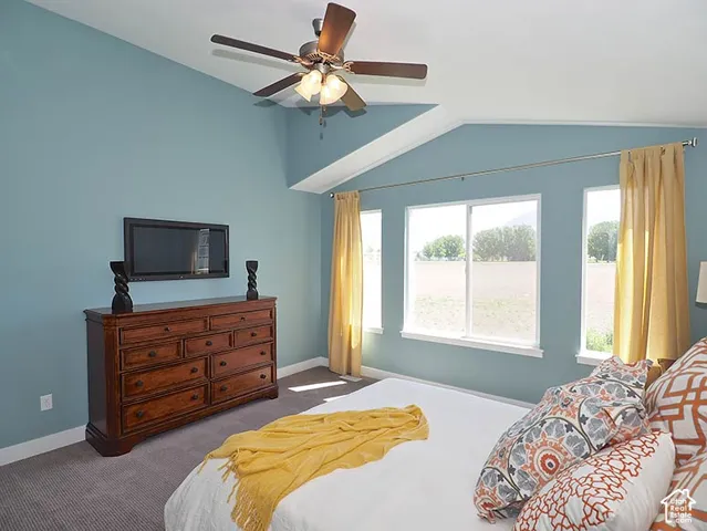 Vaulted ceiling with a ceiling fan, multiple windows with white trim, wall-mounted television, and a wood-finish dresser