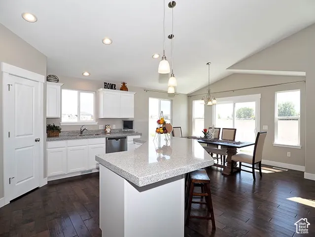 Kitchen featuring white cabinetry, light-toned countertops, a center island, wood-finish flooring, and a vaulted ceiling