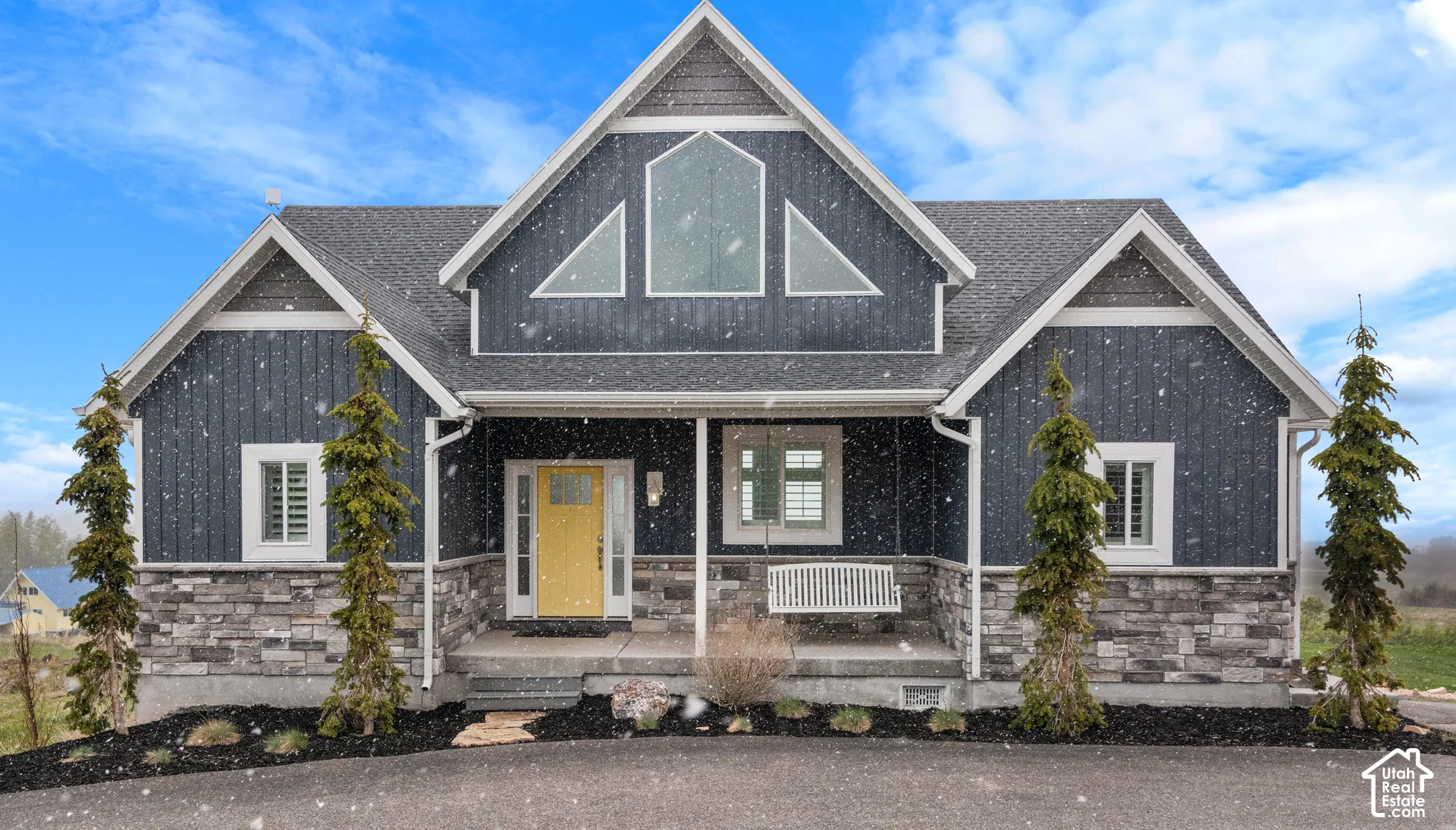 Board and batten siding with stone accents, covered front porch, and a bright yellow entry door