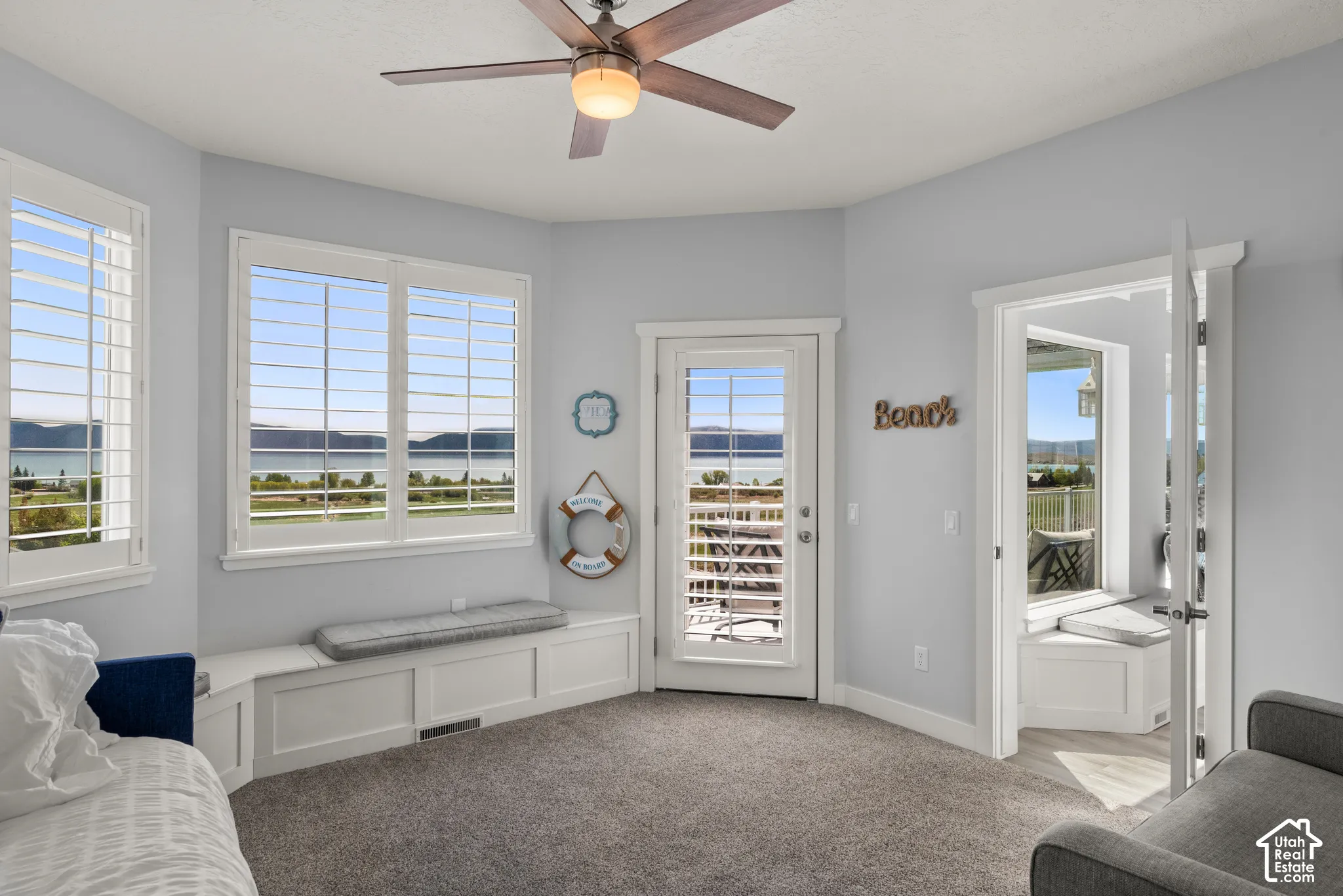 Carpeted room with a ceiling fan, white plantation shutters, and a built-in window bench