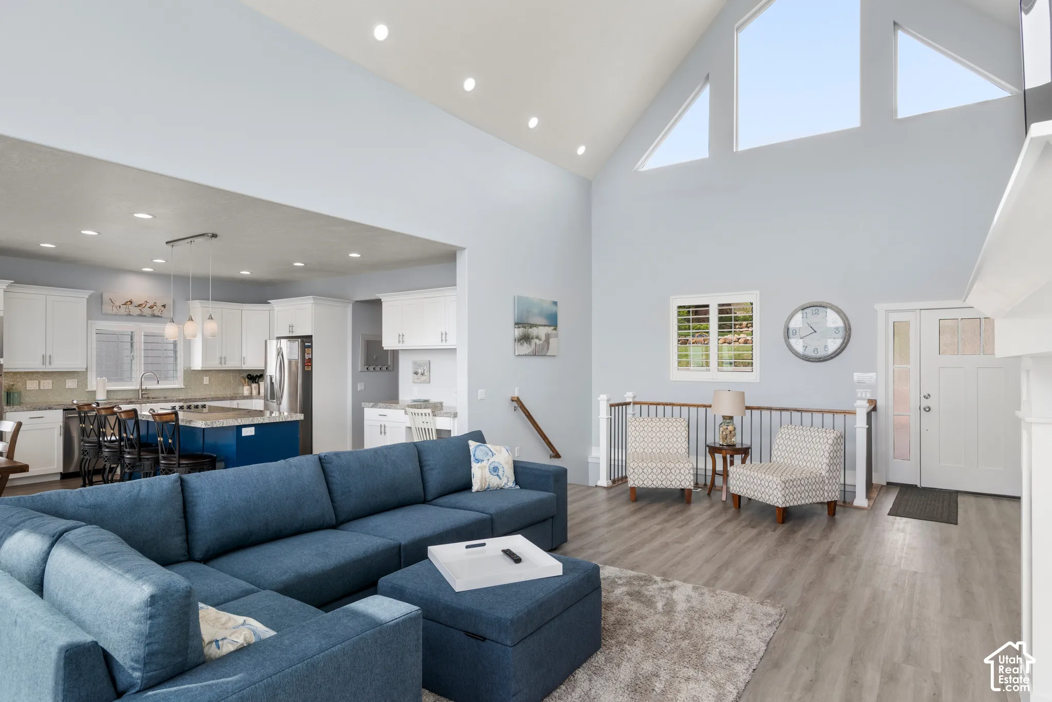 Vaulted ceilings with architectural windows, wood-finish flooring, white kitchen cabinetry, a kitchen island with seating, and stainless steel appliances