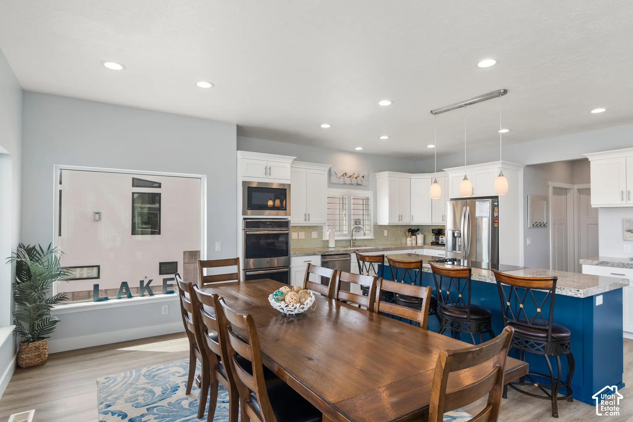 Recessed lighting, wood-finish flooring, white cabinetry, stainless steel appliances, and a blue kitchen island with a light-colored countertop