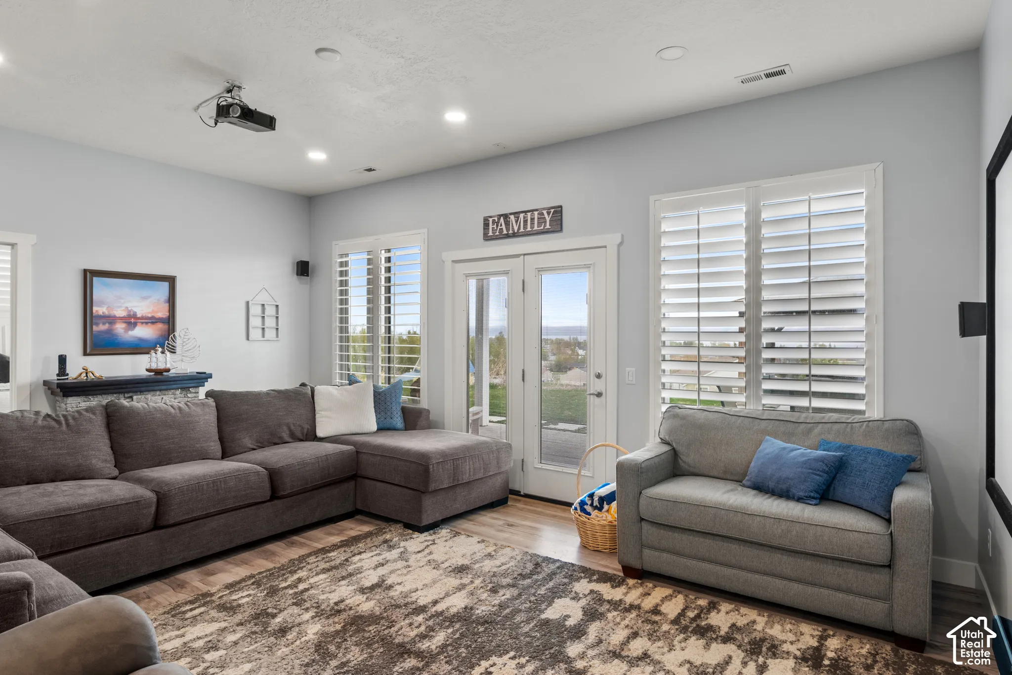 Recessed lighting, wood-finish flooring, white plantation shutters, exterior French doors, and ceiling-mounted projector