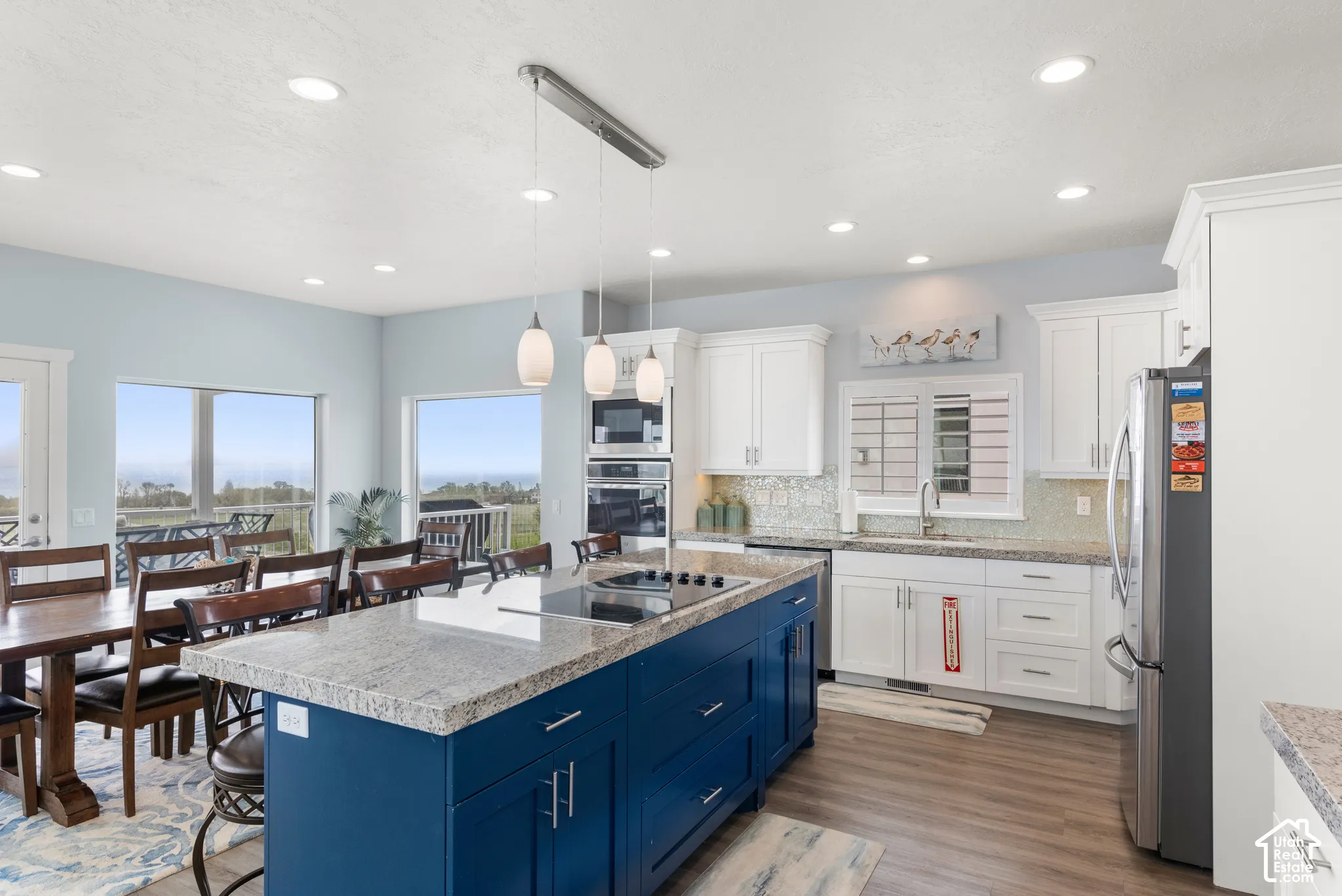 Modern kitchen featuring a blue-finished island with a cooktop, white perimeter cabinetry, stainless steel appliances, and wood-finish flooring