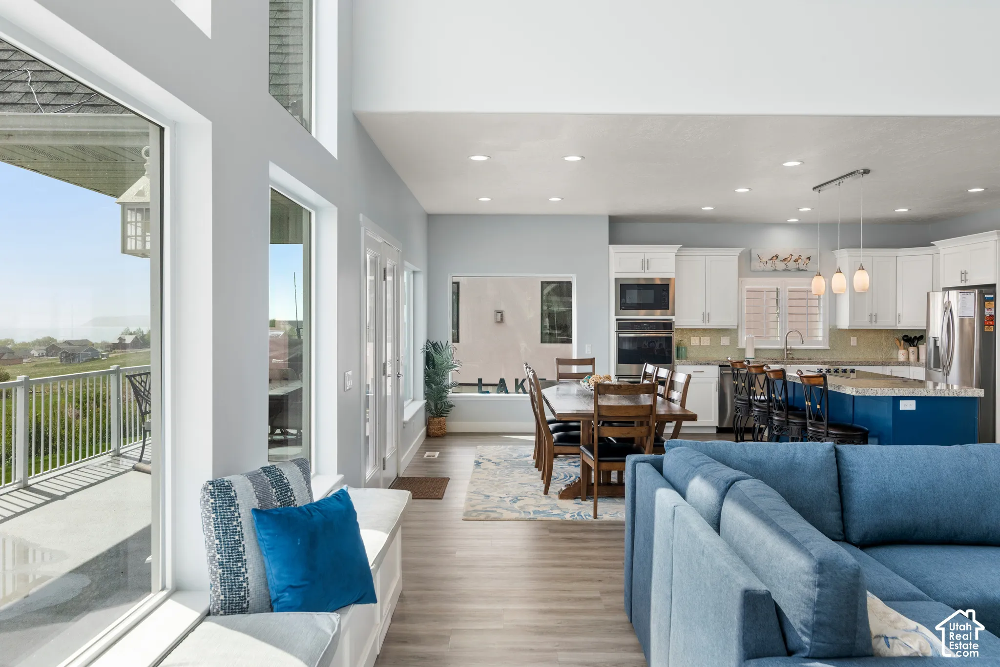 Open-concept living area with wood-finish flooring, a kitchen featuring white cabinetry and a blue island, and a built-in window bench
