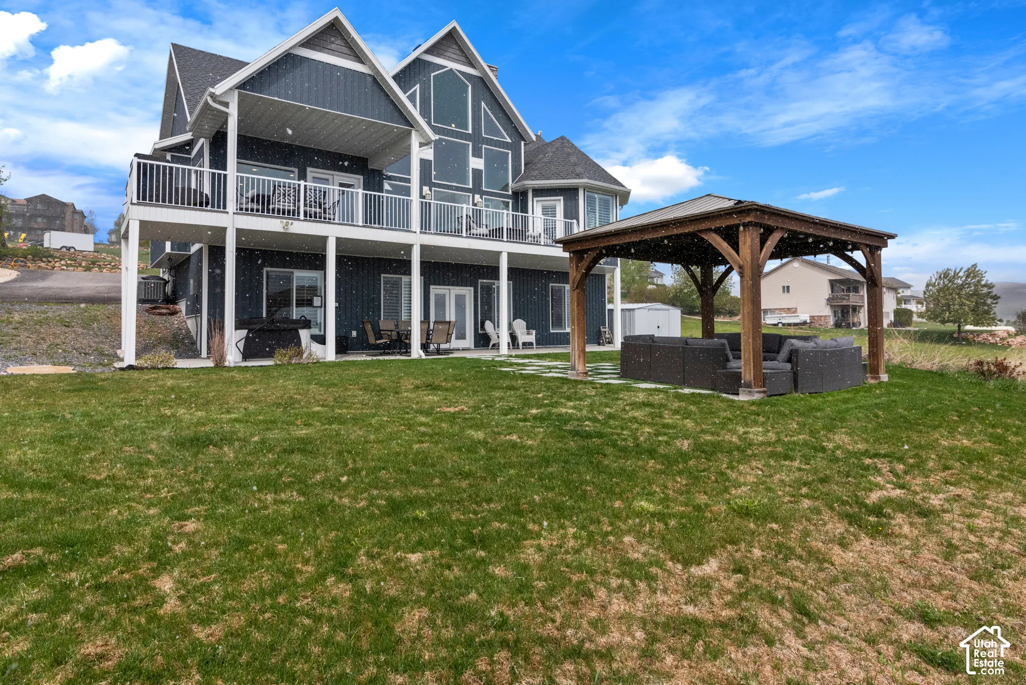 Multi-level dwelling with a gable roof, two expansive balconies with white railings, and a lower-level patio