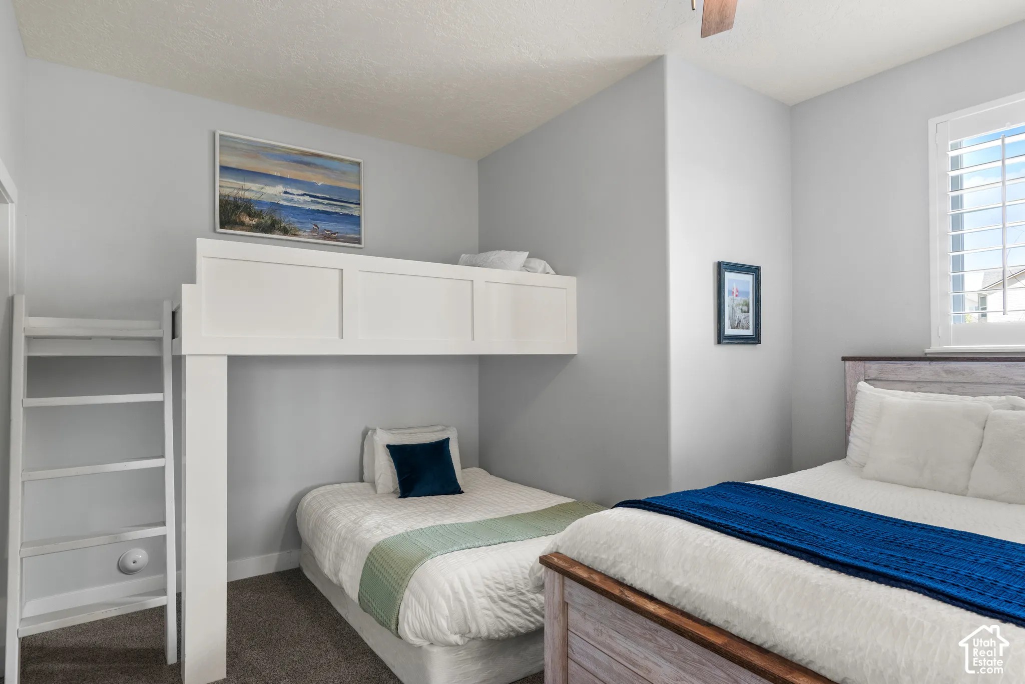 Built-in bunk bed with integrated ladder, light gray wall paint, textured carpeting, and window with white plantation shutters