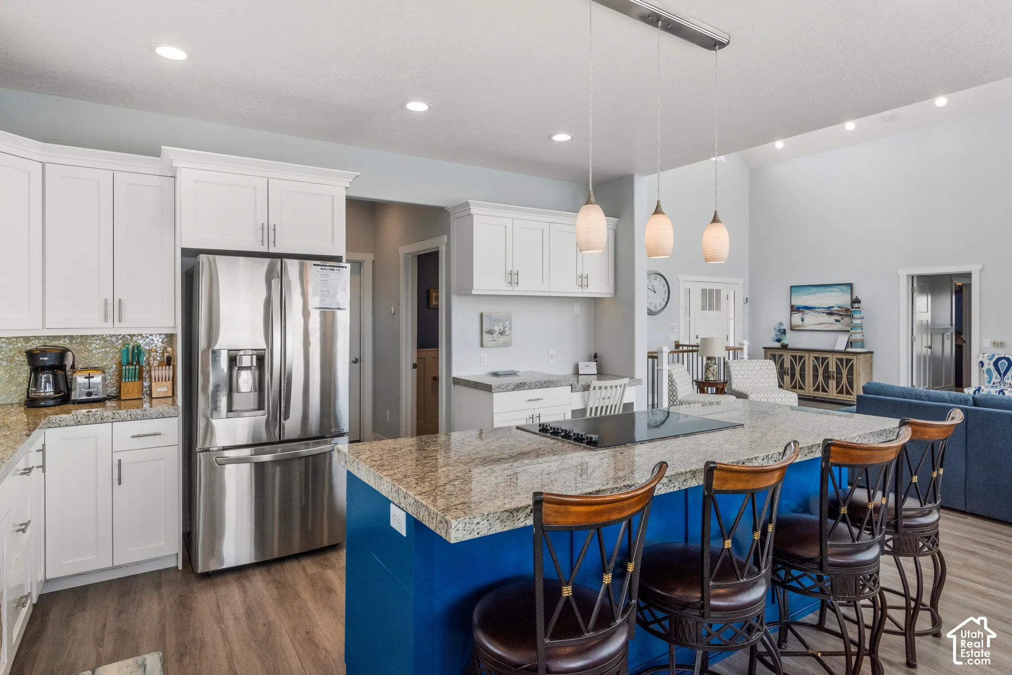 Gourmet kitchen featuring a built-in cooktop, stainless steel refrigerator, white cabinetry, granite countertops, and wood-finish flooring