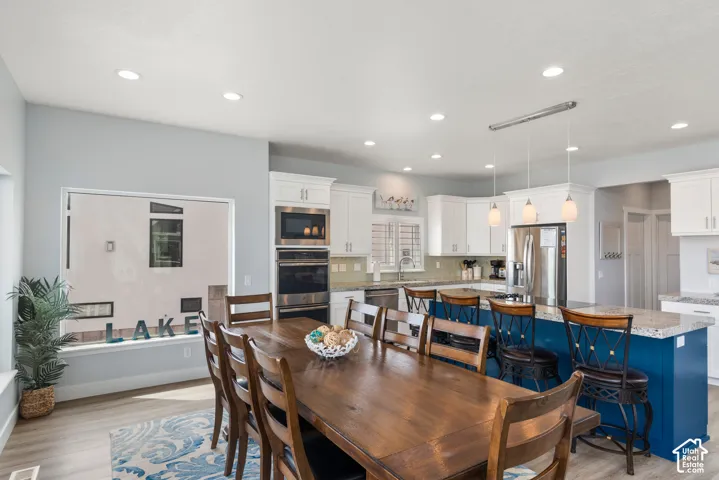 Recessed lighting, wood-finish flooring, white cabinetry, stainless steel appliances, and a blue kitchen island with a light-colored countertop