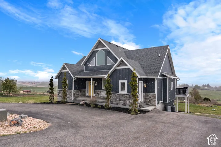 Contemporary home with dark siding and stone accents, featuring a prominent gable roofline, an arched window, and a dedicated balcony