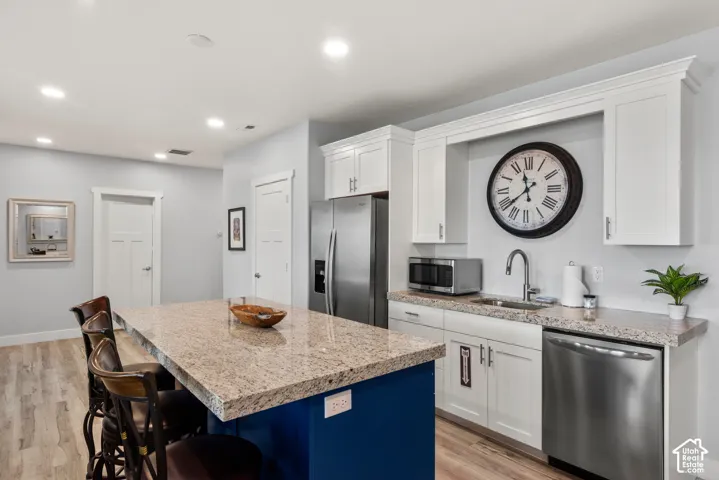 Kitchen with wood-finish flooring, white cabinetry, stainless steel appliances, and a central island with a granite-style countertop