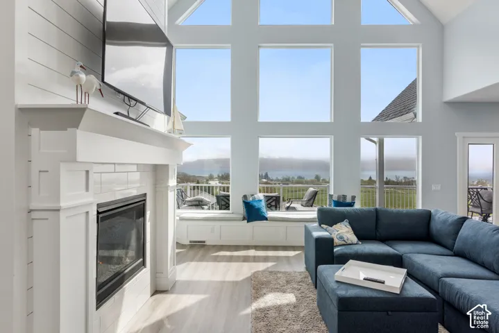 Vaulted ceiling with extensive window array, shiplap-accented fireplace with white tile surround, built-in window seating, and wood-finish flooring