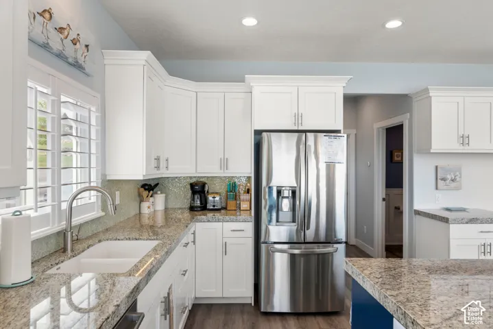 White shaker-style cabinetry with crown molding, granite countertops, a built-in stainless steel refrigerator, a double basin sink with a gooseneck faucet, and wood-finish flooring