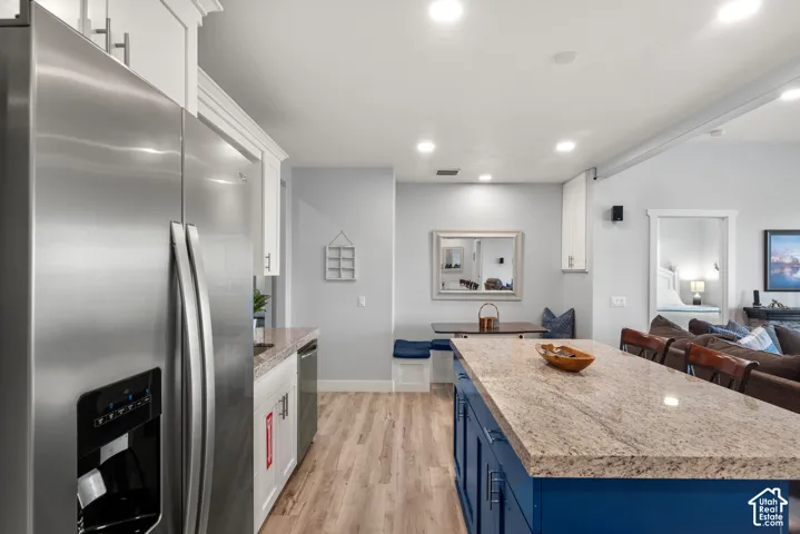 Kitchen featuring stainless steel refrigerator, white cabinetry, wood-finish flooring, recessed lighting, and a blue island with a light-toned countertop
