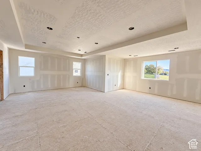Spacious unfinished room with recessed lighting, tray ceiling, multiple windows, and smooth drywall