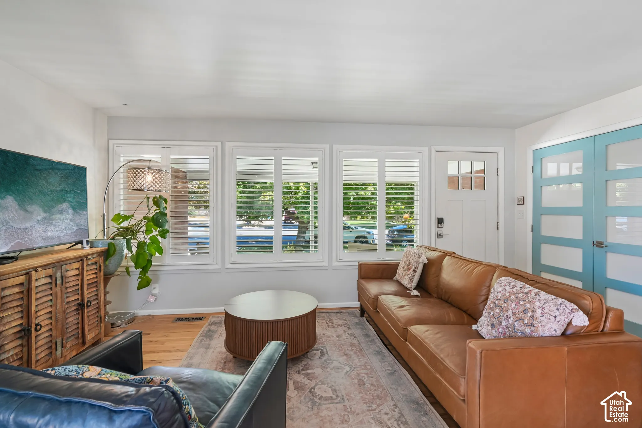 Hardwood-finish flooring, white plantation shutters, white entry door with frosted glass panes, and blue interior doors with frosted glass panels