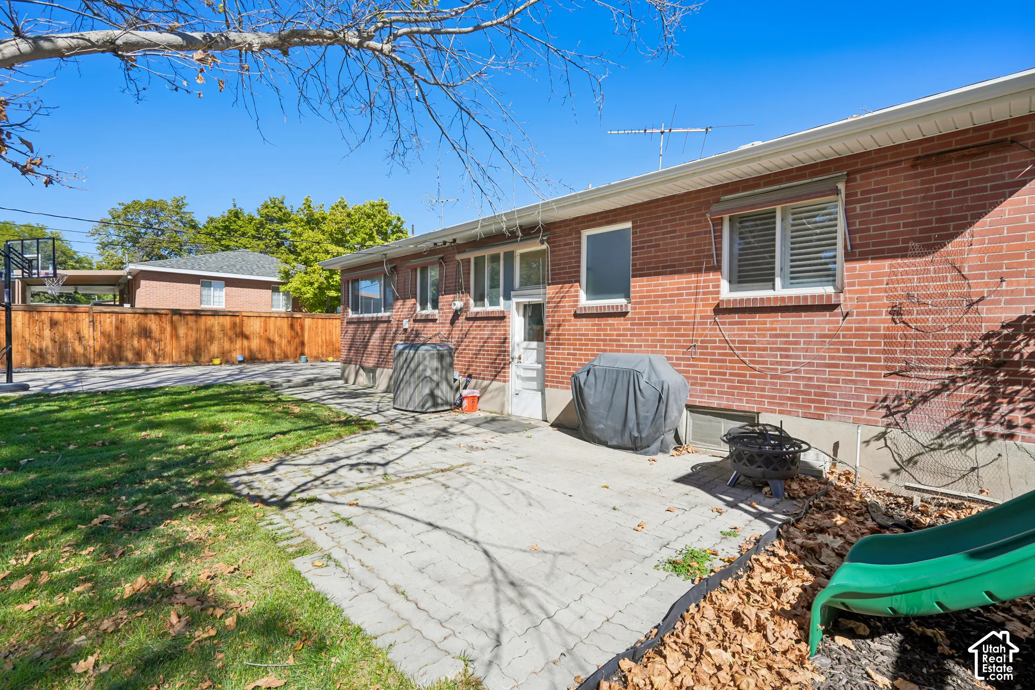 Brick ranch home with expansive concrete patio overlooking a level lawn bordered by mature trees and wooden fencing