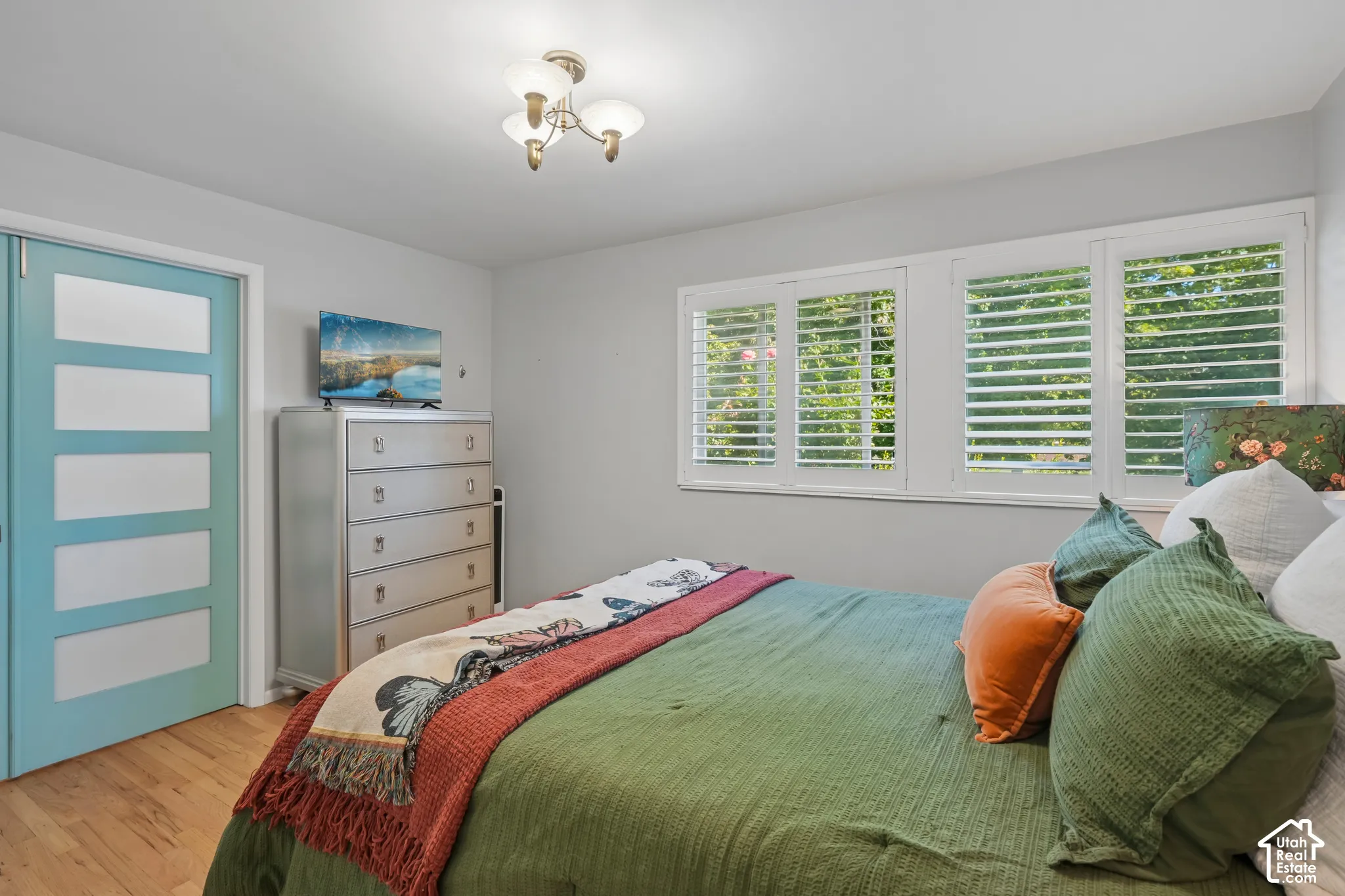 Light wood-finish flooring, a three-light ceiling fixture, and a three-panel window with white louvered shutters