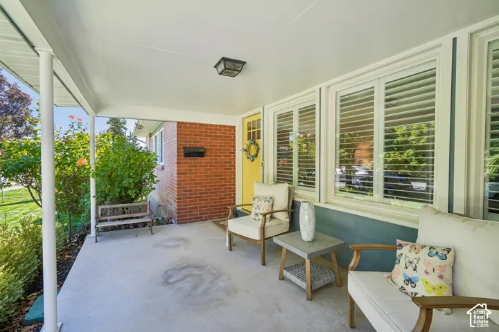 Covered front porch with a concrete surface, brick exterior, and a bright yellow entry door