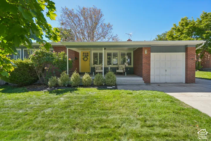 Brick and siding exterior with a covered porch, an attached single-car garage, a concrete driveway, and established landscaping