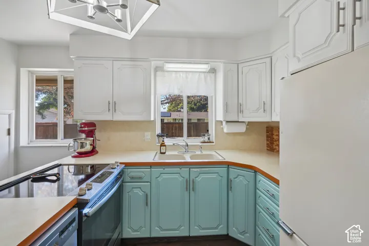 Kitchen featuring white upper cabinetry, teal lower cabinetry, a built-in electric range, a double basin sink, and wood-finish flooring