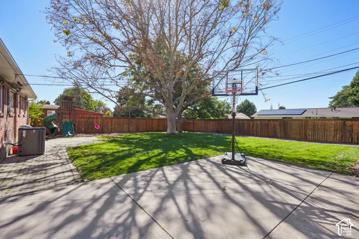 Expansive backyard featuring a mature tree, concrete patio, and a wooden fence