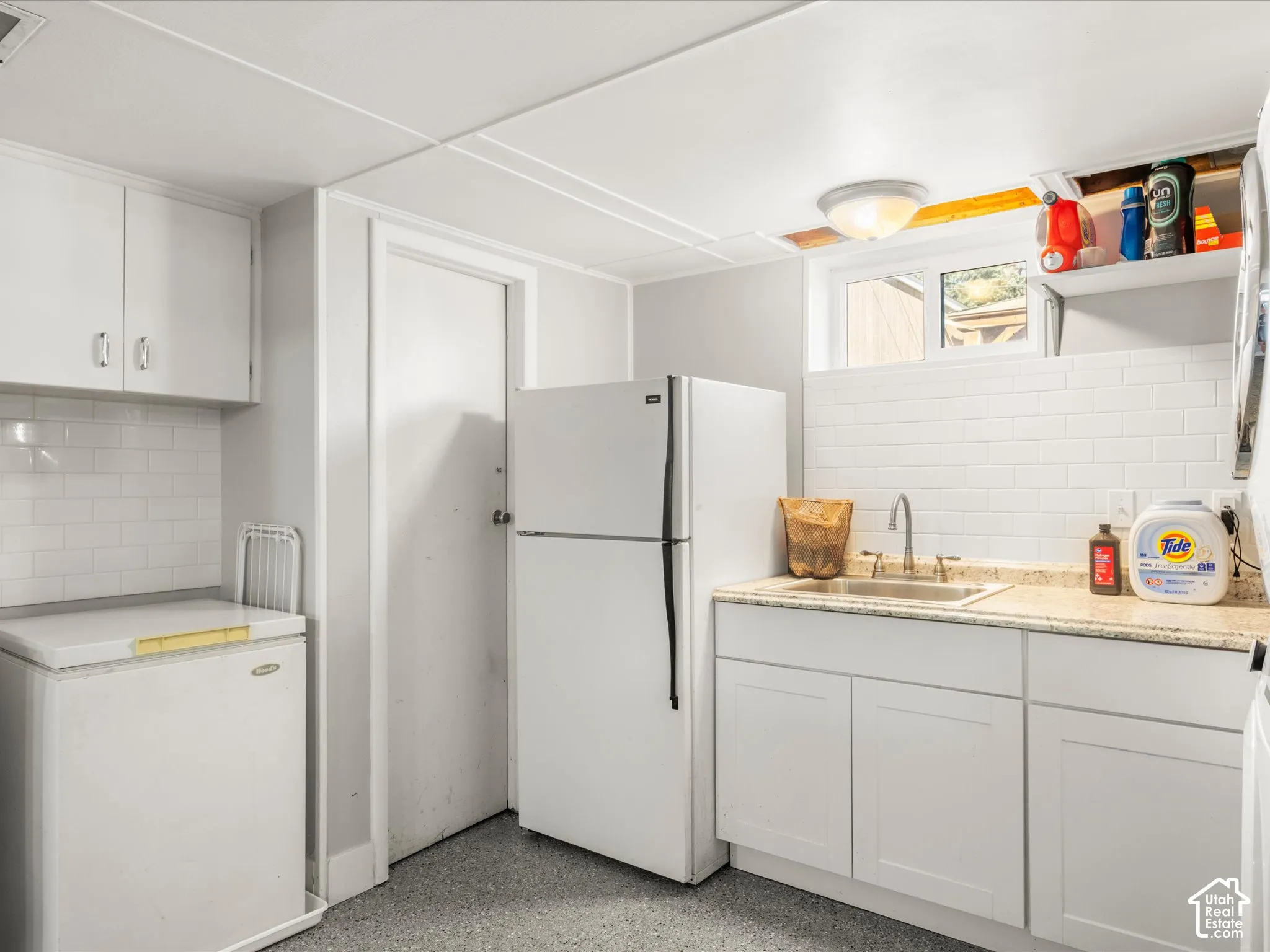 White subway tile backsplash, white cabinetry, undermount sink, light-toned countertop, and durable flooring