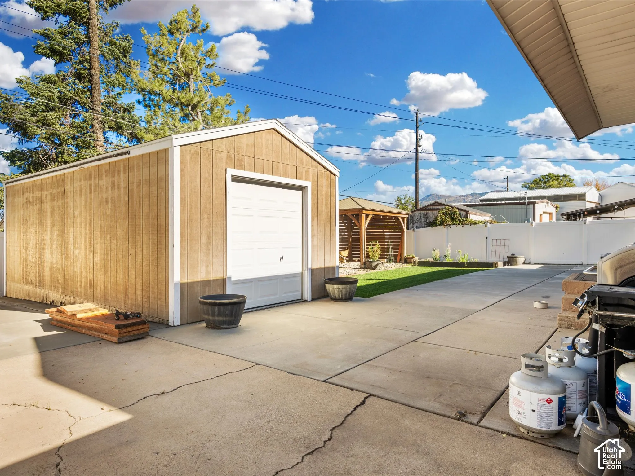 Detached storage shed with roll-up door, concrete patio, artificial turf area, and wood-finish gazebo