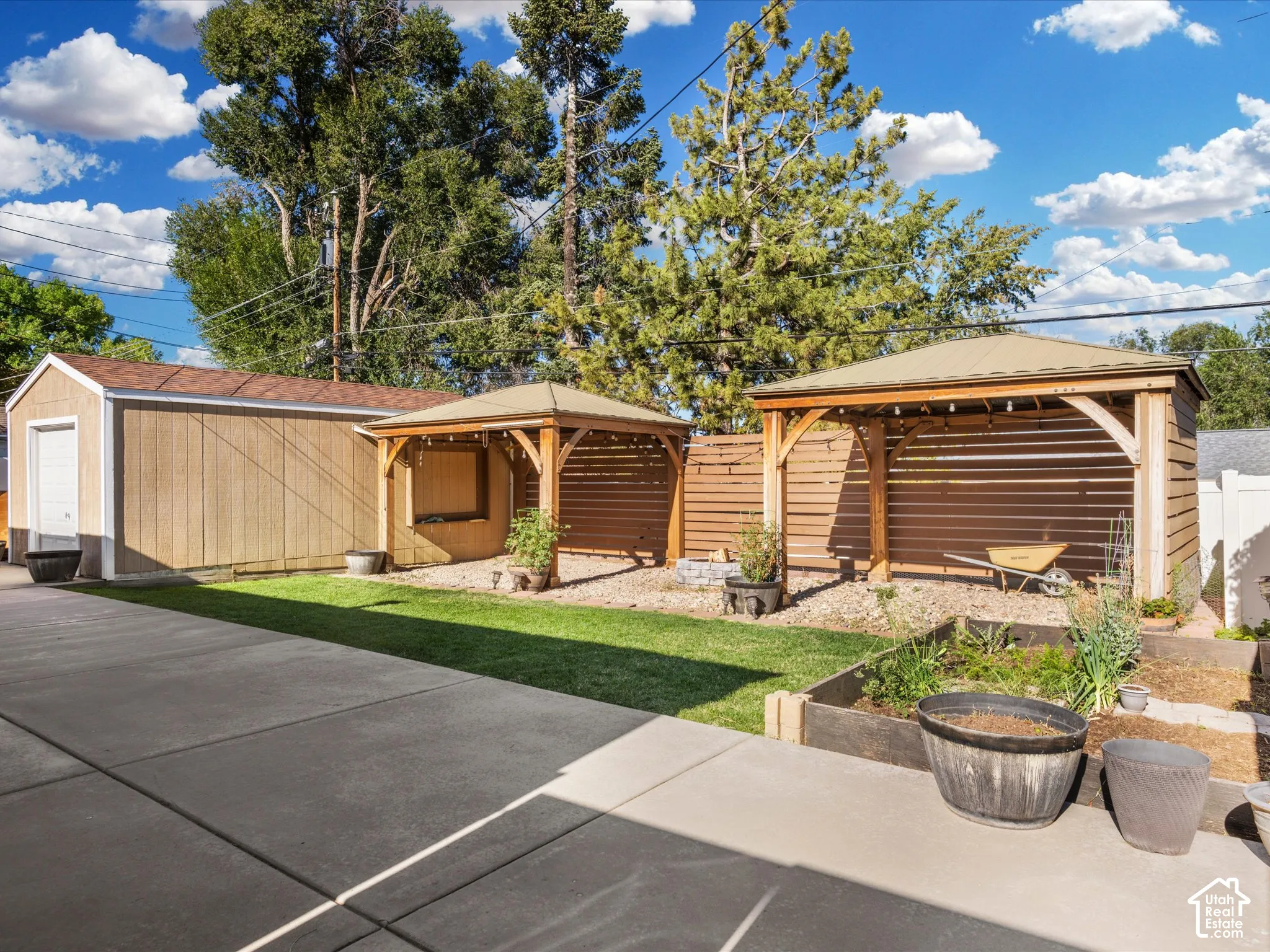 Detached garage with a roll-up door, two covered pergolas, horizontal wood privacy fencing, a raised garden bed, and a concrete patio surface