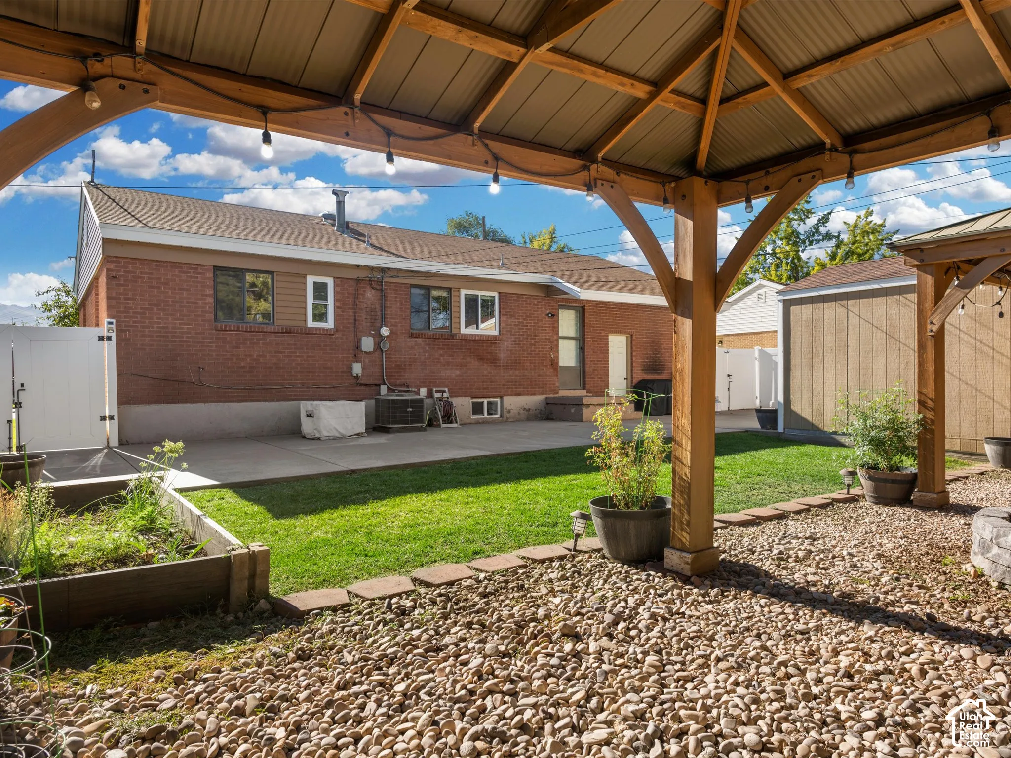 Wooden gazebo with string lighting, pea gravel ground cover, concrete patio, and fenced yard