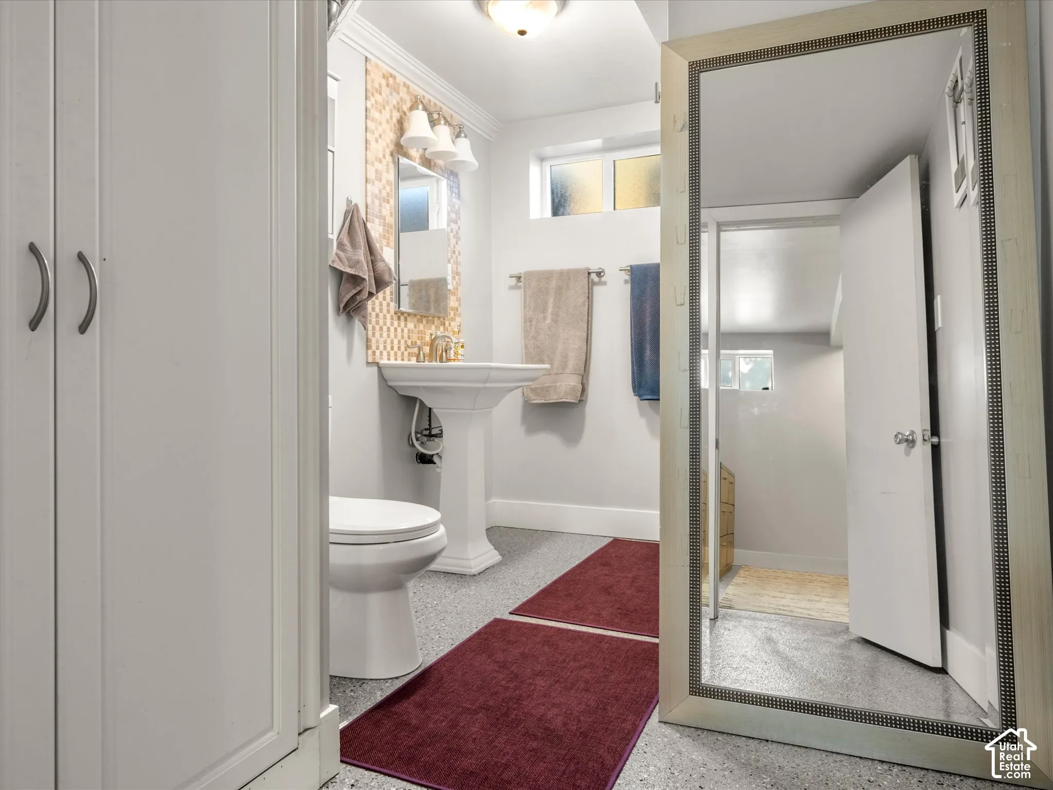 Pedestal sink with a decorative tiled backsplash and wall-mounted light fixture
