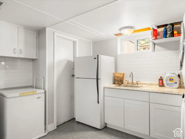 White subway tile backsplash, white cabinetry, undermount sink, light-toned countertop, and durable flooring