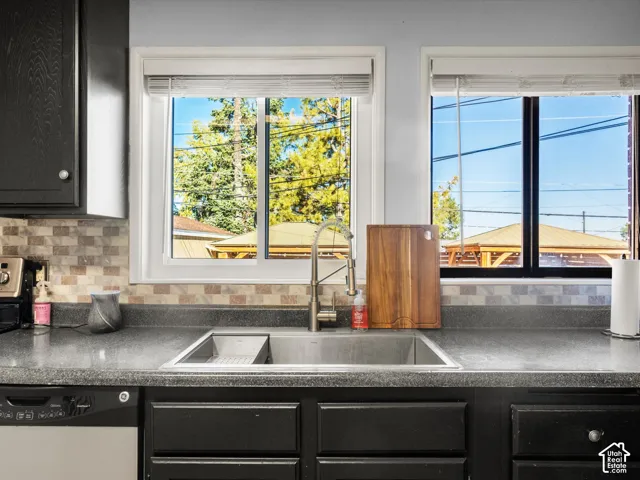 Kitchen with dark cabinetry, integrated stainless steel sink with a high-arc faucet, durable countertop, and a tiled backsplash