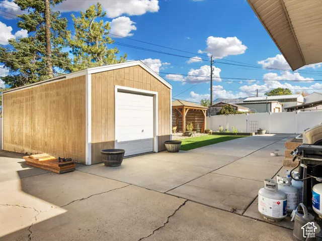 Detached storage shed with roll-up door, concrete patio, artificial turf area, and wood-finish gazebo