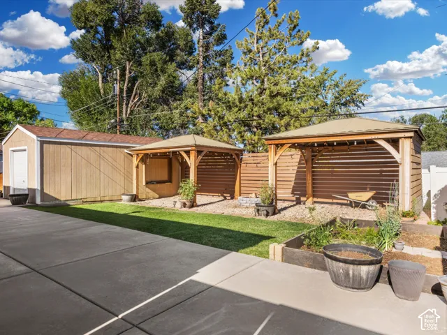 Detached garage with a roll-up door, two covered pergolas, horizontal wood privacy fencing, a raised garden bed, and a concrete patio surface